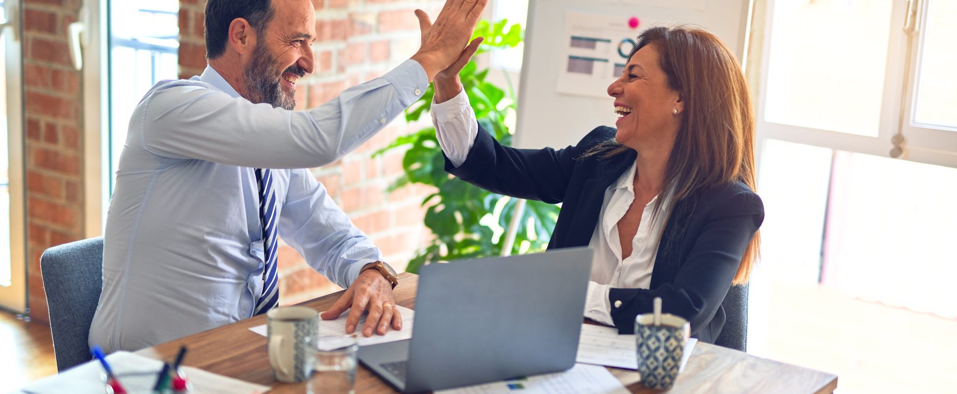 Two professionals celebrate success with a high five at a desk