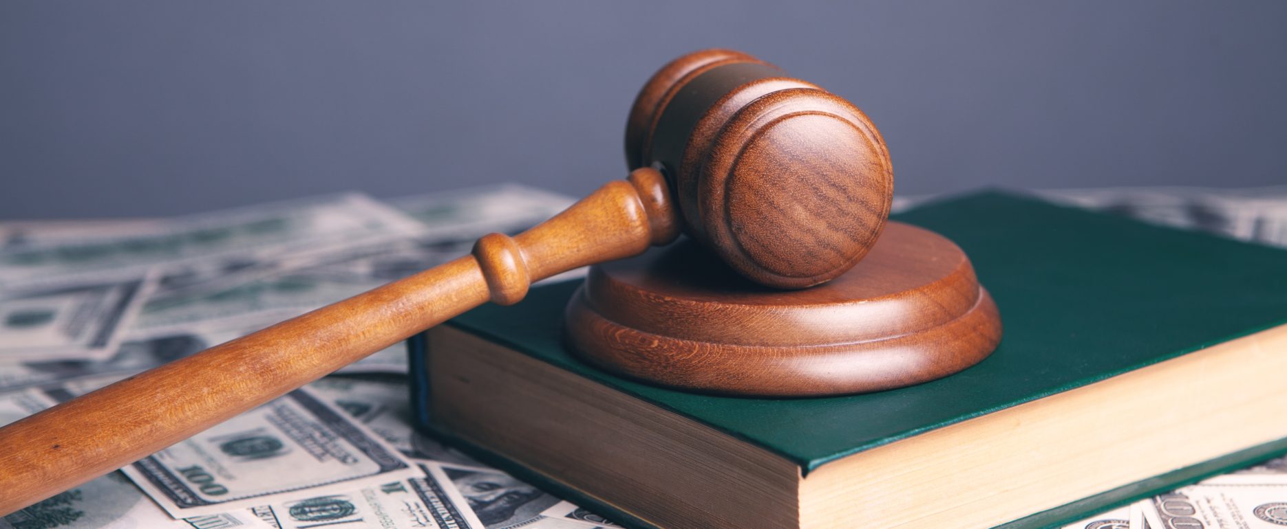 A judge's gavel rests over a book on a stack of money