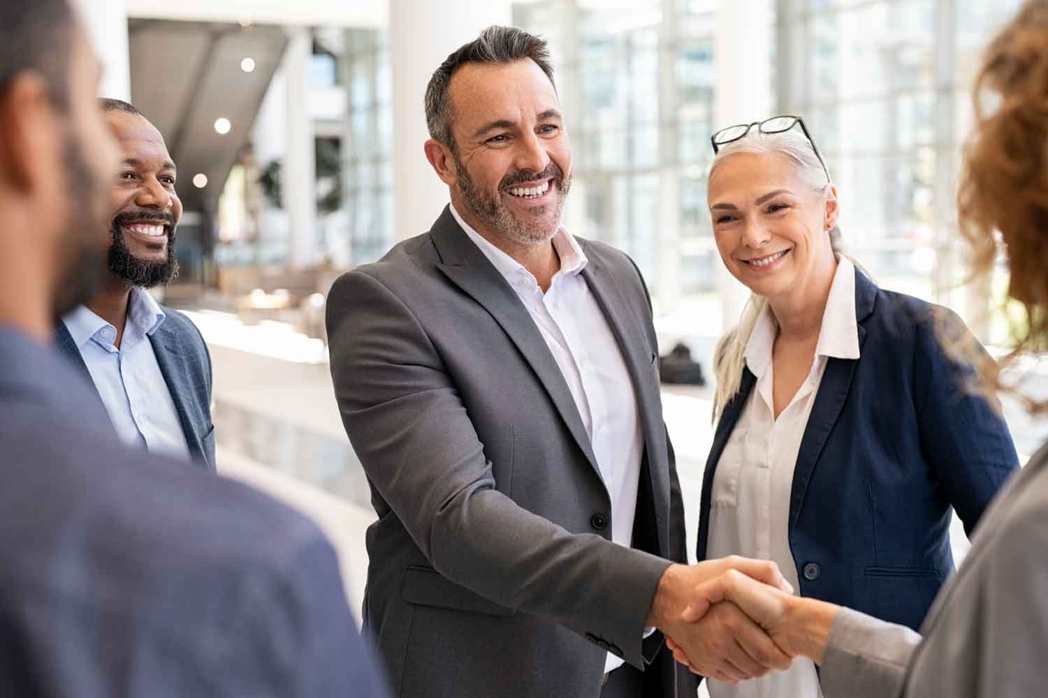 mature businessman shaking hands with businesswoman around a group of people