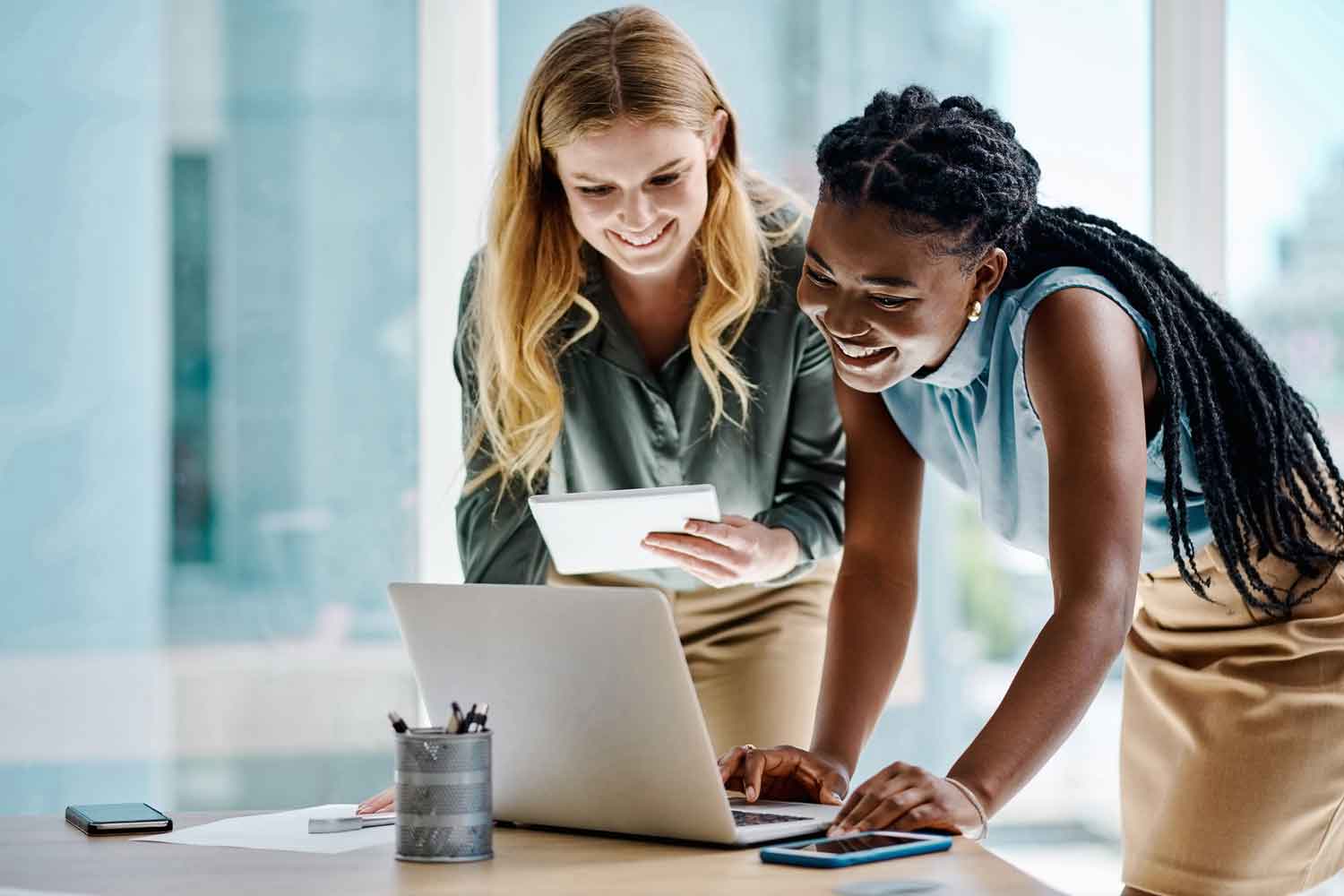 Two businesswomen working together on a digital tablet and laptop in an office