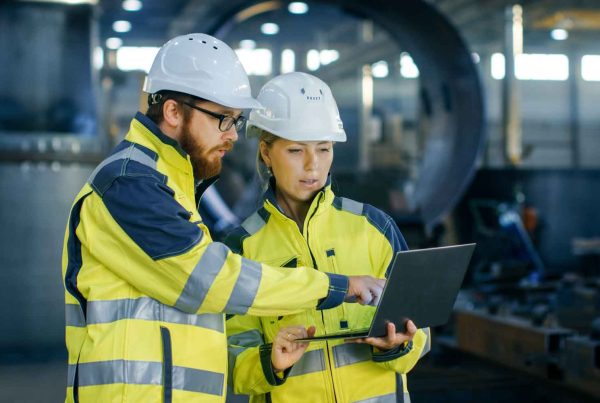 Male and Female Industrial Engineers in Hard Hats Discuss while Using Laptop