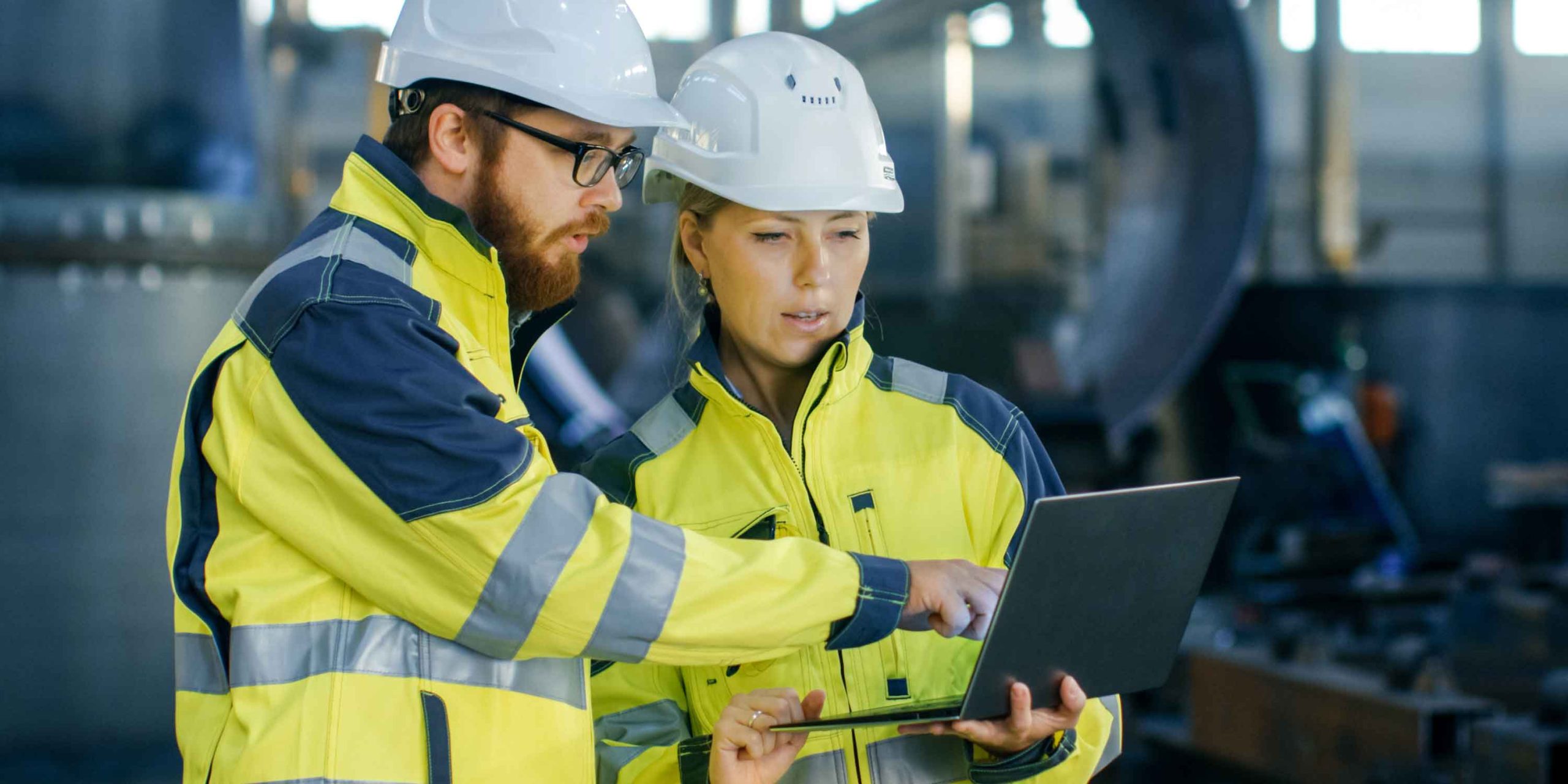 Male and Female Industrial Engineers in Hard Hats Discuss while Using Laptop